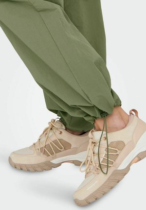 Beige Sport Schuhe mit Mesh- und Wildlederakzenten, strukturierten Sohlen und hellen Schnürsenkeln, kombiniert mit lockeren, olivgrünen, tapered Hosen.