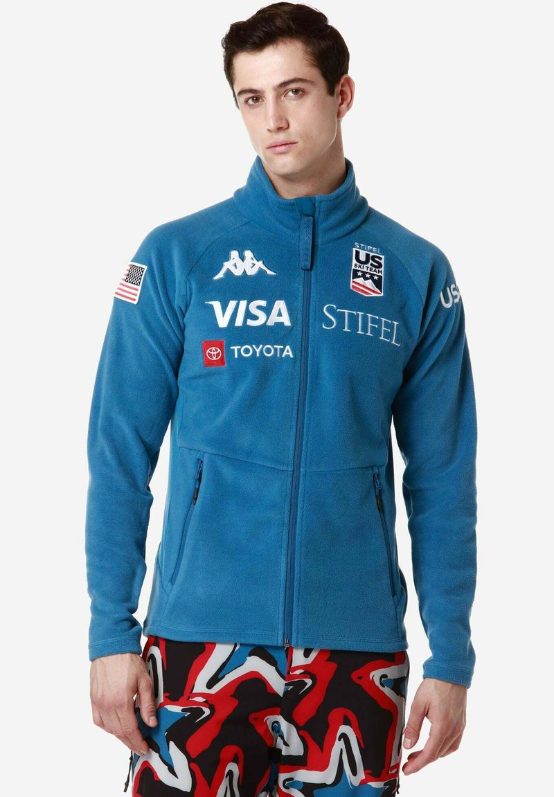 Giacca in pile blu da uomo con zip frontale, due tasche laterali e loghi. Presenta polsini elastici e colletto alto.