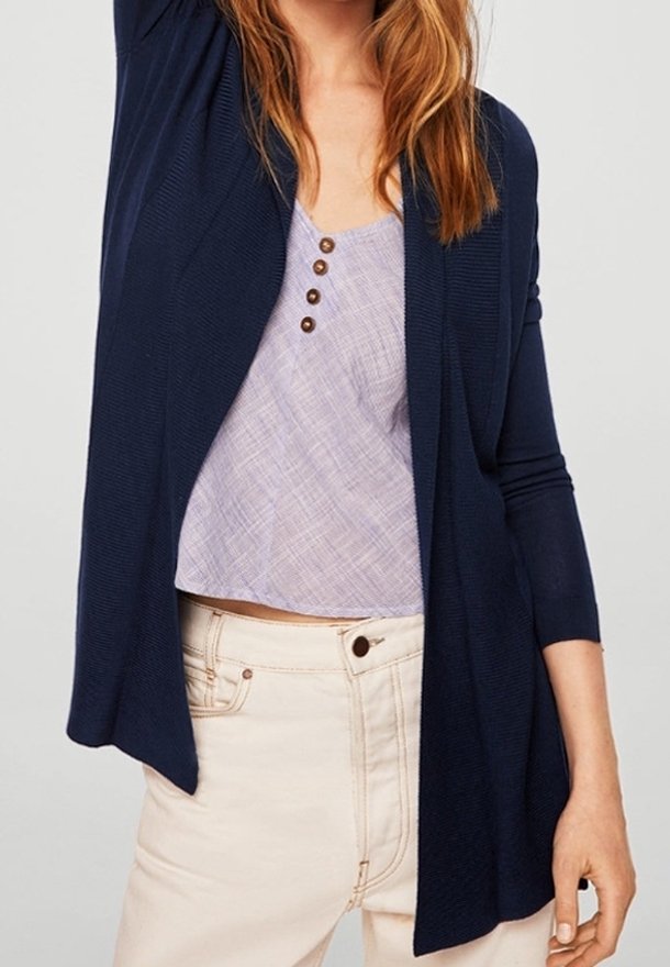Femme portant un cardigan bleu marine ouvert devant, sur un haut violet clair à boutons, associé à un pantalon beige taille haute.