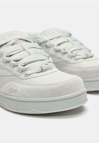 Sneaker grigie chiare realizzate in pelle e scamosciato con lacci testurizzati e suola in gomma. Il design presenta cuciture e un logo discreto sul lato.