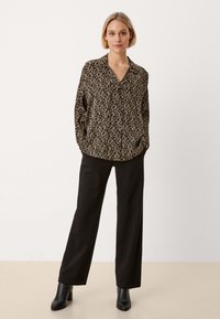 Blusa nera e beige a motivo con scollo a V e maniche lunghe, abbinata a pantaloni neri a gamba larga e stivaletti neri con tacco.