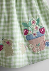 Tela de cuadros verdes y blancos con ratones bordados en beige y crema, fresas rojas, flores blancas y una maceta rosa con hojas verdes.