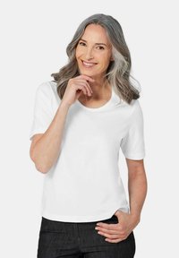 Weißes Baumwoll-T-Shirt mit kurzen Ärmeln, rundem Ausschnitt und lässigem Schnitt. Getragen mit dunklen Jeans. Glatte Textur.