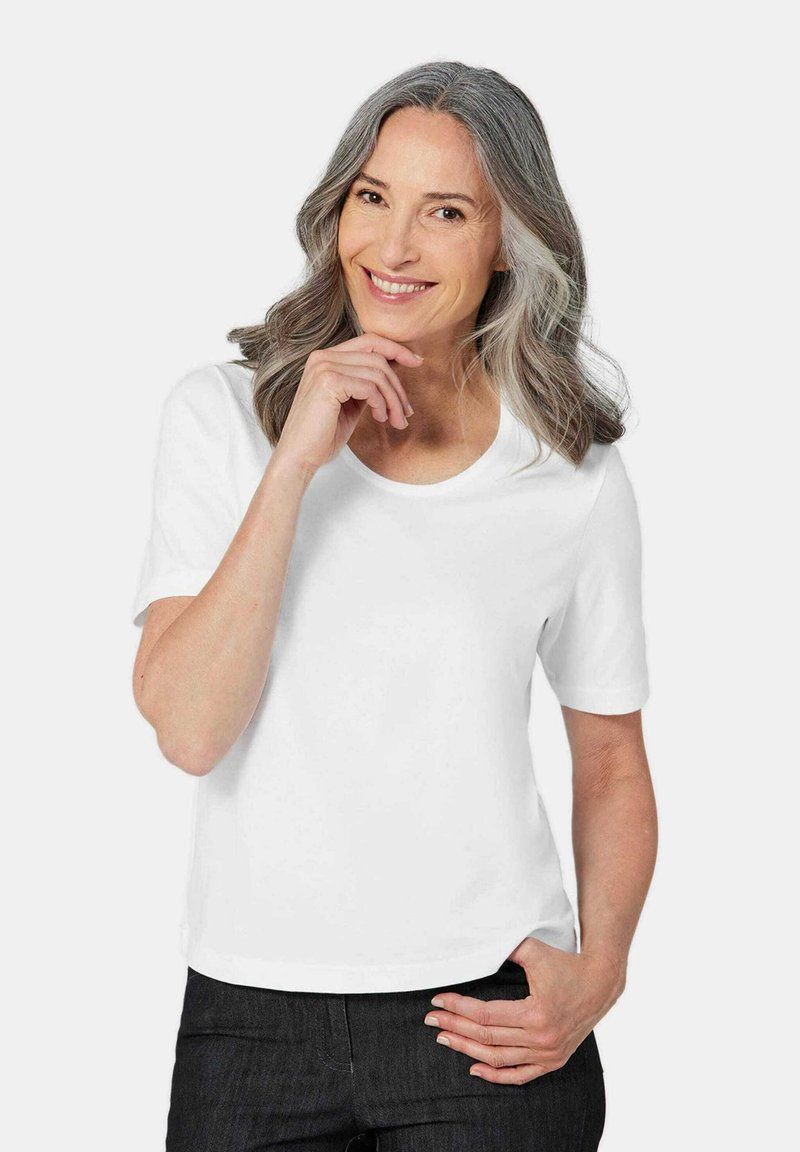 Weißes Baumwoll-T-Shirt mit kurzen Ärmeln, rundem Ausschnitt und lässigem Schnitt. Getragen mit dunklen Jeans. Glatte Textur.