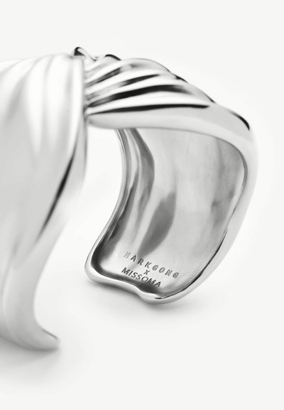 Bracelet manchette en argent poli avec des crêtes en relief et gravé "MARKGONG x MISSOMA" à l'intérieur du bracelet sur fond blanc.