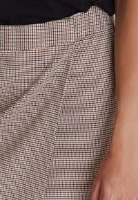 Un tissu à carreaux marron et noir présente un design plissé avec une texture lisse. La taille est plate et soigneusement cousue.