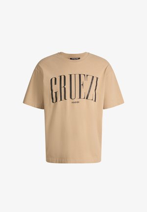 Beige T-shirt met korte mouwen met zwarte gebogen tekst "GRUEZI" en kleinere "HABIBI" eronder gedrukt op de voorkant.
