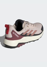 Light pink athletic shoe with black accents, textured mesh upper, three pink stripes, red pull tab, and a rubber outsole for traction.