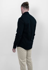 Heren langemouwen shirt in donker marineblauwe stof, slim fit met knoopmanchetten, gecombineerd met lichtbeige broek. Glad oppervlak, klassiek kraagontwerp.
