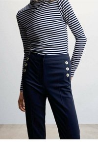 Pantalons taille haute marine avec cinq boutons dorés sur le côté, associés à un haut ajusté à rayures marines et blanches à manches longues.