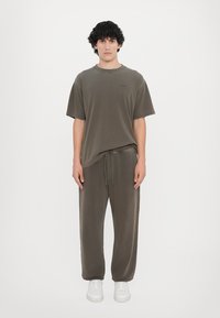 Oliven grøn t-shirt med korte ærmer og rund hals, parret med matchende snorede bukser. Hvide sneakers fuldender outfittet. Blød tekstur.