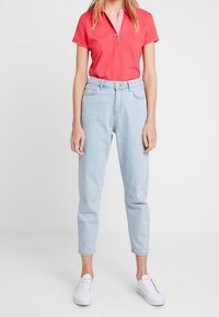 Rotes Polohemd mit kurzen Ärmeln und Kragen, hellblaue High-Waist-Jeans und weiße Sneaker. Glatte Textur, lässige Passform.