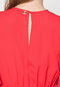 Red dress with a keyhole back featuring a gold hardware detail at the neck, made of soft, smooth fabric. Feminine cut with flowing sleeves.