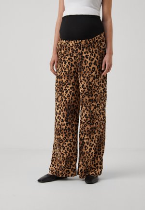 Zwangere persoon die luipaardprint wijde zwangerschapsbroek met zwarte elastische tailleband en zwarte puntige schoenen draagt.