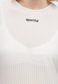 Zbliżenie osoby noszącej białą prążkowaną koszulkę z czarnym napisem "sportful" w pobliżu kołnierzyka.