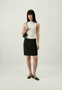 Saia preta até ao joelho combinada com uma t-shirt branca canelada. A modelo segura uma pequena mala preta e usa sapatilhas pretas com uma tira.