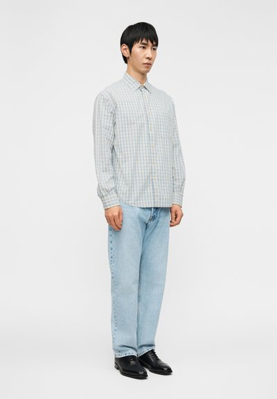 Ανοιχτό μπλε καρό πουκάμισο με κουμπιά, μακριά μανίκια, συνδυασμένο με ανοιχτό μπλε τζιν και μαύρα παπούτσια. Απλός σχεδιασμός με απαλή υφή υφάσματος.