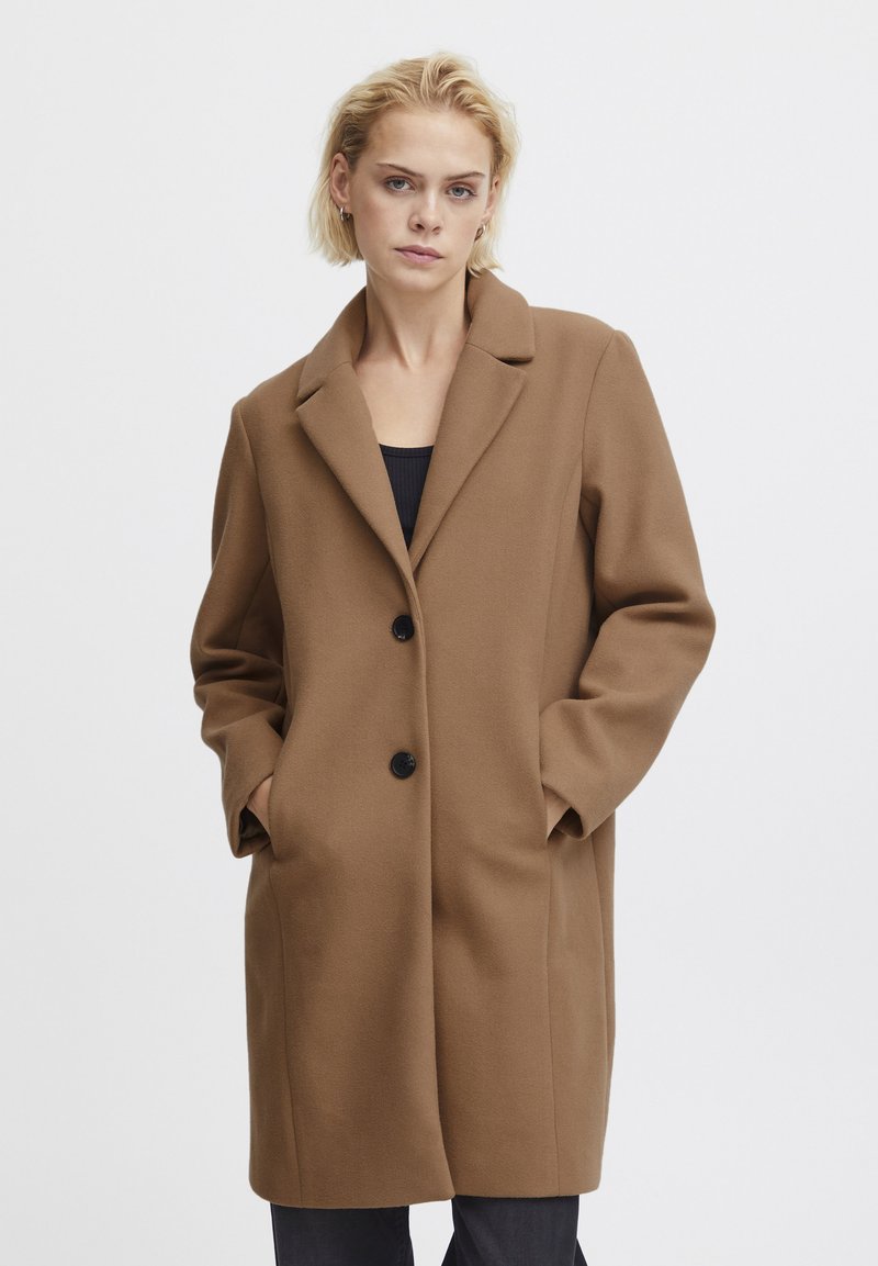 Cappotto in misto lana marrone con colletto a punte, due bottoni neri e tasche laterali, caratterizzato da una linea dritta e un tessuto leggermente testurizzato.