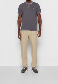 Szara koszulka polo z krótkim rękawem, z haftowanym logo na piersi, zestawiona z beżowymi lnianymi spodniami i ciemnymi sneakersami. Gładka faktura tkaniny na całej powierzchni.