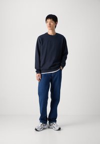 Námornícky crewneck sveter, voľný strih, z bavlneného zmesi; v kombinácii s voľnými modrými džínsy a bielymi teniskami s čiernymi akcentmi.