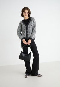 Grijze en zwarte gestreepte cardigan met knopen, gedragen over een zwarte top en gecombineerd met zwarte broeken en een zwarte handtas. Glanzende flats maken de look compleet.