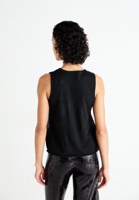 Top negro sin mangas de corte relajado, con escote redondo y espalda texturizada. Combinado con pantalones negros brillantes de lentejuelas.