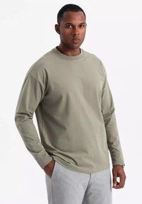 Camiseta de manga larga verde claro, hecha de algodón suave, con cuello redondo y corte relajado, combinada con pantalones en gris claro.