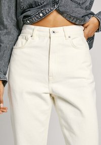 Högmidjade, ljuskrämfärgade jeans i denim, med framfickor, synlig sömnad och en något avsmalnande bendesign.