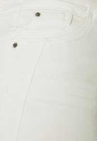 Jeans de mezclilla blanca con una textura suave, con un bolsillo frontal y herrajes negros contrastantes. La costura es sutil y uniforme.