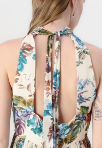 Robe à dos nu avec motif floral, fabriquée en tissu léger aux couleurs vives de bleu, violet, orange et vert.