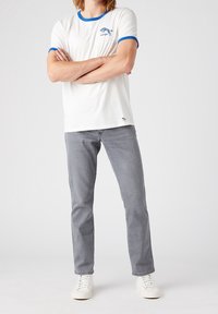 Vit t-shirt med blå ringkrage, med en liten blå grafik på bröstet. Matchas med grå jeans och vita sneakers.