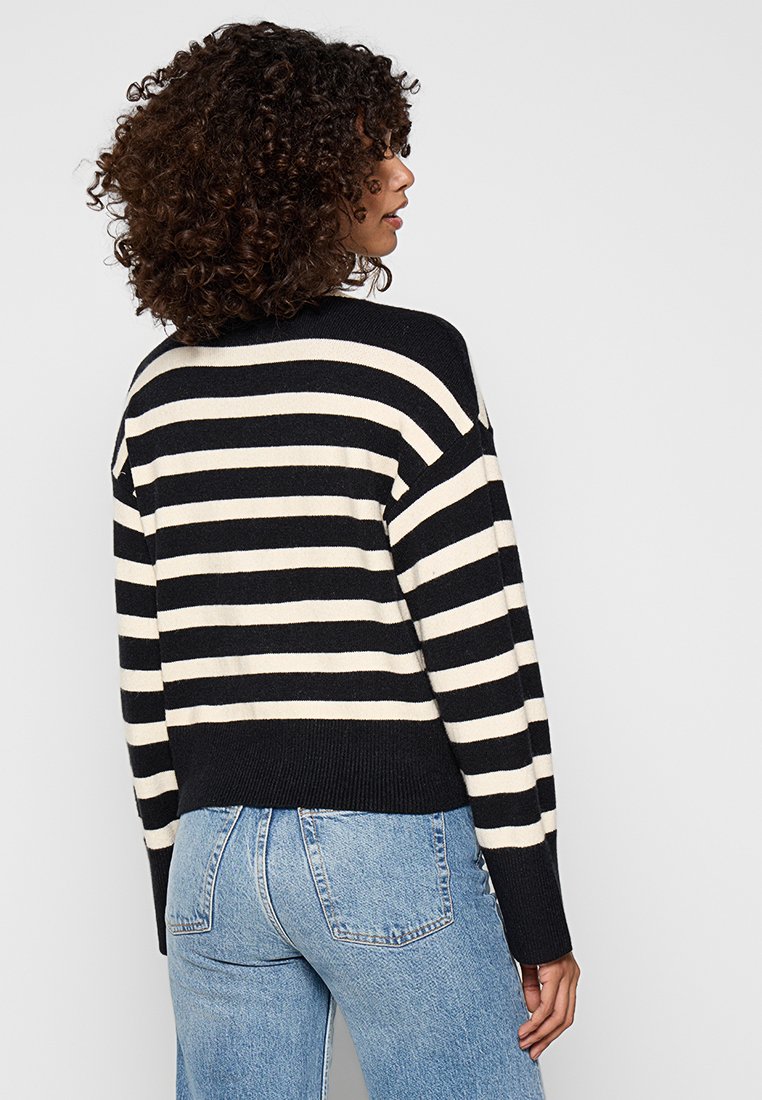 Czarny i kremowy sweter w paski z luźnym krojem, z obniżonymi ramionami i prążkowanym dołem. W zestawie z jasnoniebieskimi dżinsami.