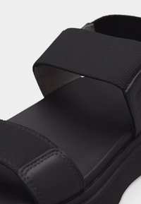 Μαύρο σανδάλι με φαρδιές υφασμάτινες λουρίδες και μαλακό πέλμα, σχεδιασμένο για άνεση και καθημερινή χρήση.