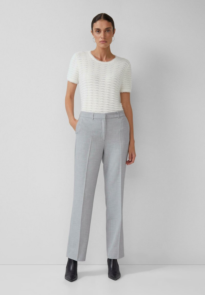 Haut en tricot texturé blanc à manches courtes associé à un pantalon tailleur gris. Des bottes à talons aiguilles noires viennent compléter le look. Design simple et épuré.