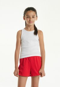 Bílý žebrovaný nátělník s kulatým výstřihem v kombinaci s červenými bavlněnými šortkami. Tento outfit se vyznačuje volným střihem a jemnou texturou.