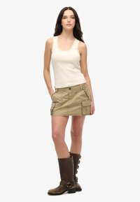 Beige tanktop met kantafwerking, gecombineerd met een kaki cargorok met zijzakken. Bruine leren kniehoge laarzen met banddetail.