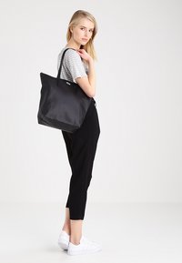 Borsa a tracolla nera con due manici robusti, realizzata in tessuto morbido. Presenta un design minimalista con un ampio interno e nessun hardware visibile.