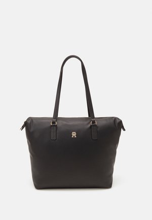 Sort læder tote taske med lange håndtag og et lille gyldent logo centreret foran, mod en ensartet lys baggrund.
