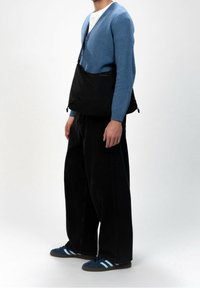 Černá kabelka přes rameno s elegantním designem, nošená přes světle modrý cardigan, doplněná volnými černými kalhotami a námořnickými botami s modrými pruhy.