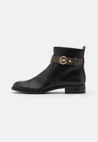 Botte chelsea en cuir noir avec un petit talon, ornée d'une sangle à motifs marron et d'un détail logo circulaire doré sur le côté.