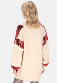 Maglione oversize lavorato a maglia color crema con accenti in paillettes rosse sulle maniche. Maniche lunghe e ampie con finitura testurizzata. Semplice silhouette strutturata.