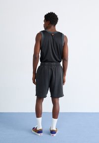 Svart trenings tanktop med blå kanter, matchende svarte shorts og mønstrede joggesko. Ensfarget bakgrunn og innendørs miljø.