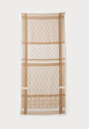 Écharpe beige à motifs avec des designs géométriques et floraux, dotée d'une texture douce et de bords à franges. Le texte du logo est intégré dans le motif.