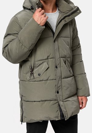 Homme portant une doudoune d’hiver vert olive avec capuche, fermeture éclair et boutons sur le devant, et poches à rabat obliques.