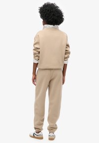 Beige Sweatshirt- und Jogginghosen-Set aus weichem Material. Das Sweatshirt hat ein kurz geschnittenes Design und eine lockere Passform; die Hose verfügt über elastische Bündchen.