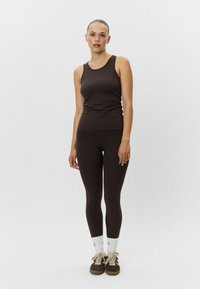 Hnedý tielko a zodpovedajúce legíny z elastického materiálu. Má jednoduchý dizajn bez vzorov, nosené s bielymi ponožkami a hnedými topánkami.