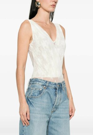 Donna che indossa un top senza maniche in pizzo bianco con scollo a V infilato in jeans a vita alta azzurri, arricchito da grandi orecchini rotondi dorati.