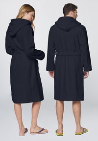 Navy blue, hooded bathrobes with long sleeves and belt. Soft texture, knee-length, pockets on either side. Worn with flip-flops.