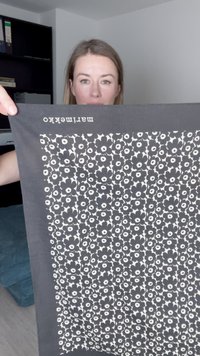 Črna tkanina z belim cvetličnim vzorcem in okroglimi oblikami. Na vrhu je besedilo "marimekko" natisnjeno v belem.