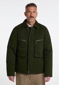 Mørkegrøn jakke med krave-design, to lynlåslommer på brystet og et slidstærkt stof. Den har en knaplukning fortil og lange ærmer.
